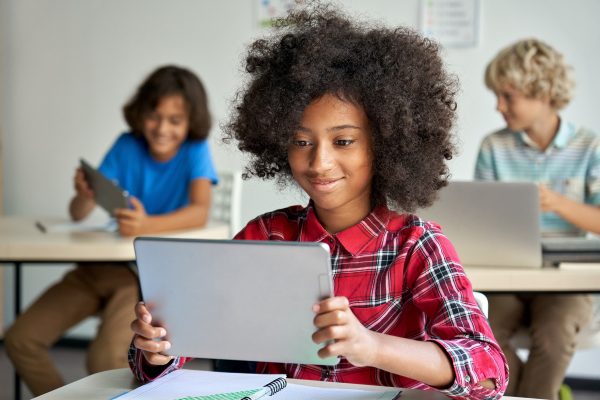 Happy African teen school girl holding device using digital tablet computer at class in classroom. Smiling black junior school student learning online education program app technology during lesson.; Shutterstock ID 2036186231; purchase_order: 4090M50 561099; job: Oxford Placement Test marketing C Hurling; client: ELT; other: Inside